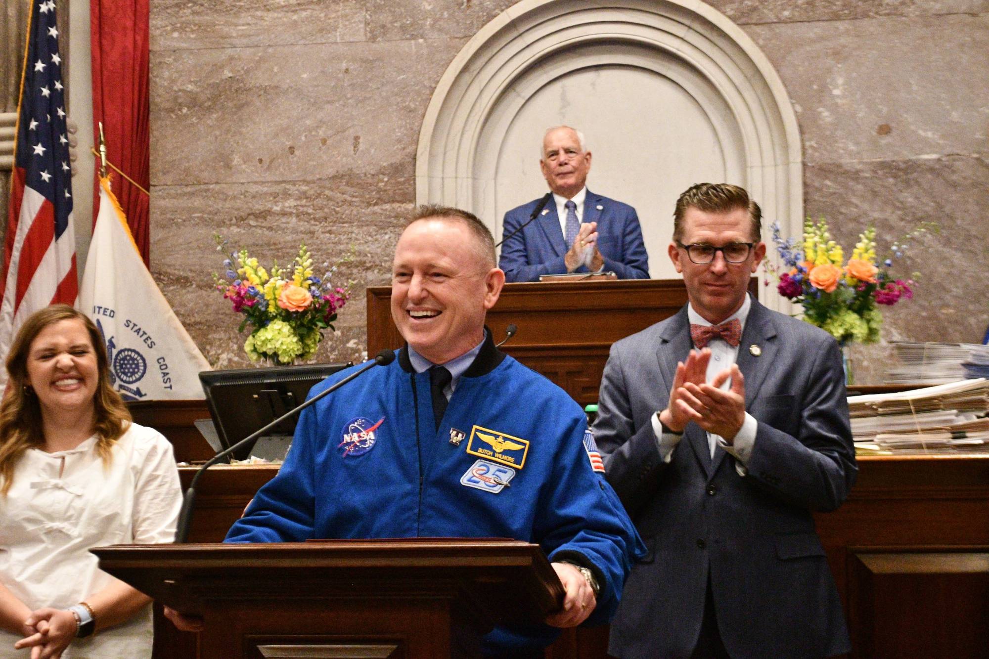 Wilmore in a blue NASA jacket at a wooden podium at the state capital.