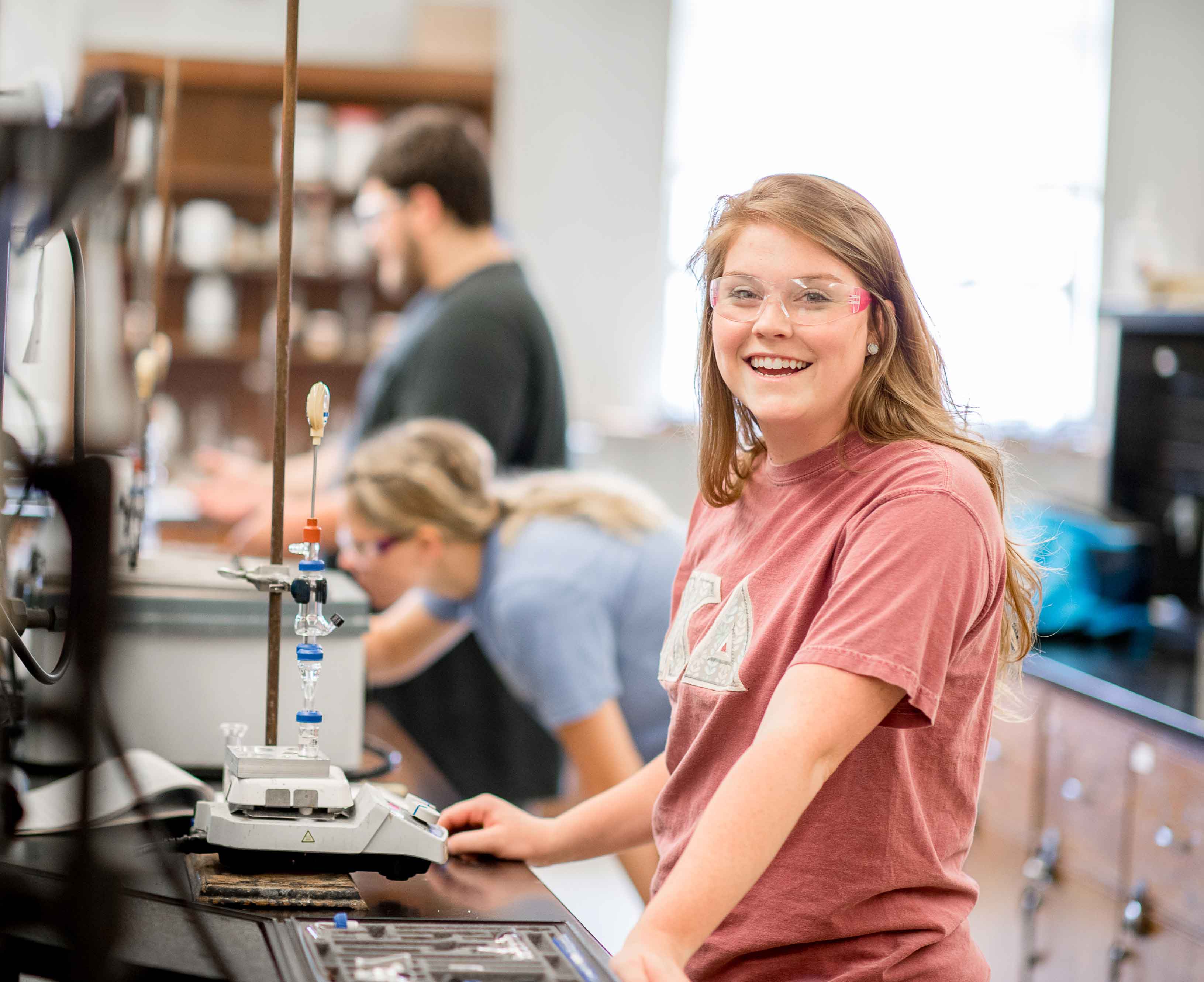 A female student in a chemistry lab smiling at the camera.