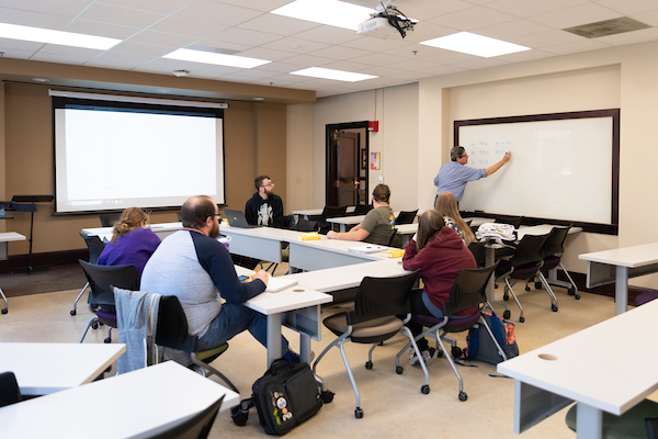 Professor at front of class writing on whiteboard