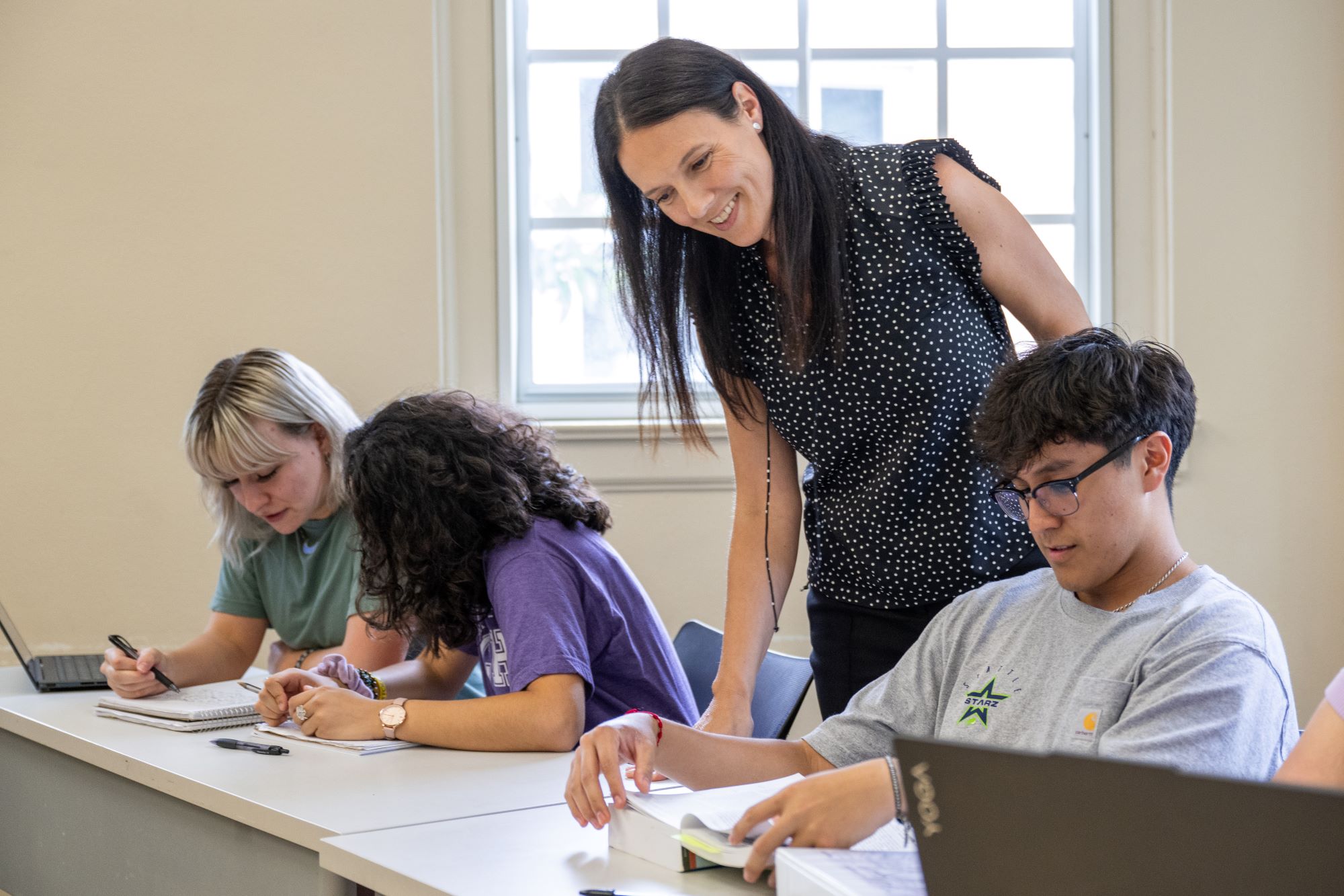 Professor of Spanish teaching students sitting at desks in front of windows
