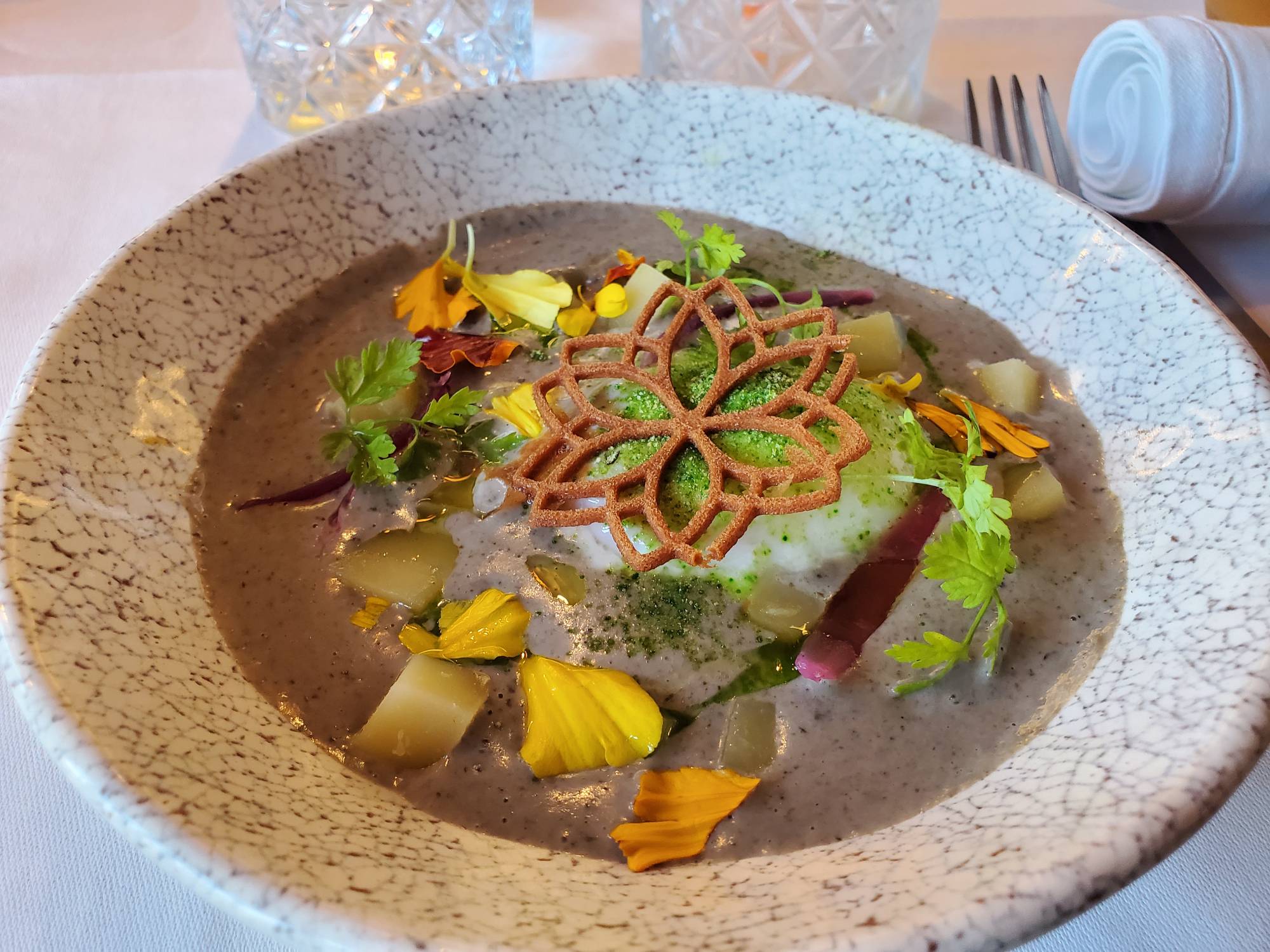 a bowl of soup with elaborate garnishes of flower petals, cilantro, and a cracker pressed into the shape of a flower