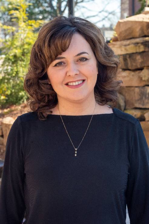 Brunet Caucasian female wearing a dark shirt with a short neckless.