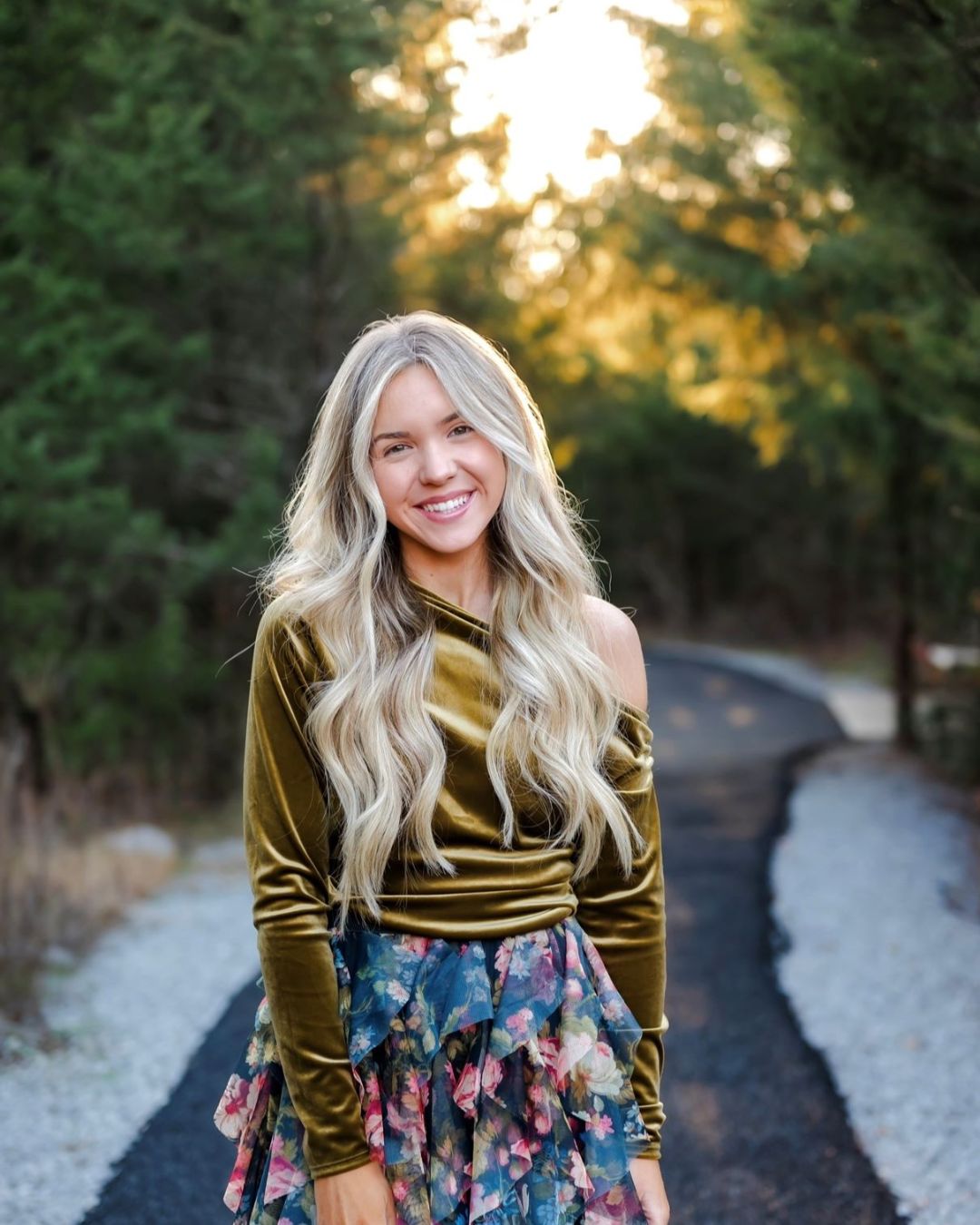 a woman standing on a road smiling wearing a velvet long sleeve and skirt