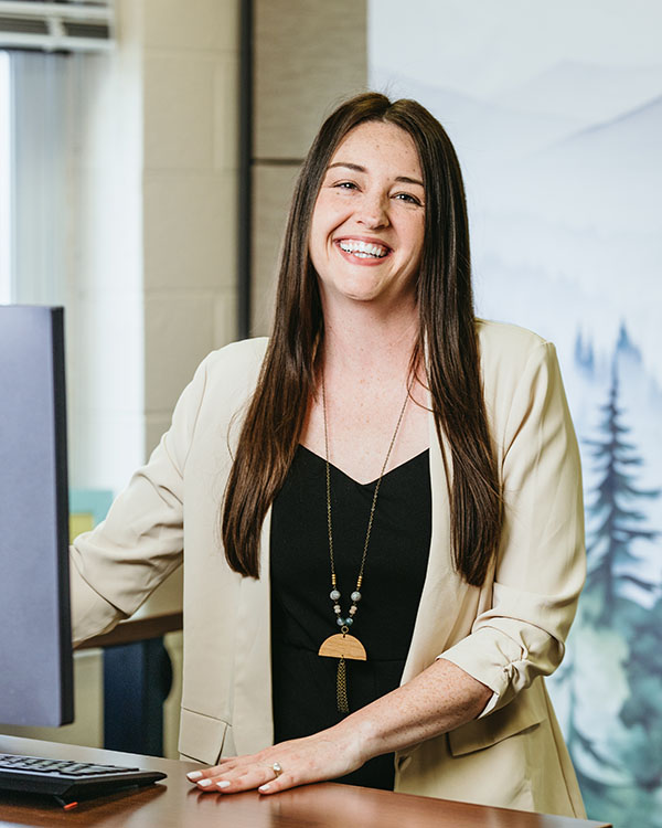 Portrait of Mallory Matthews standing at a desk and smiling.