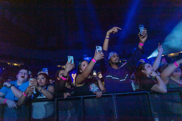 A groupf of students at a SOLO concert handing on the guard railing leading up to the stage.