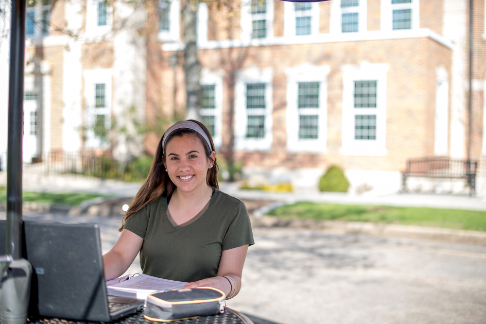 student with computer sitting outside on the quad.