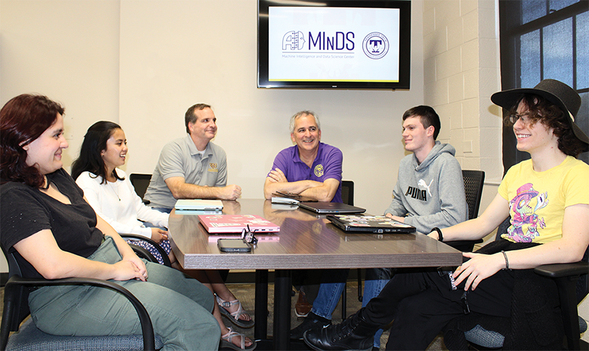 Group of professors and students gather around a table.