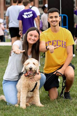 Two students and a dog giving Wings Up to the camera.