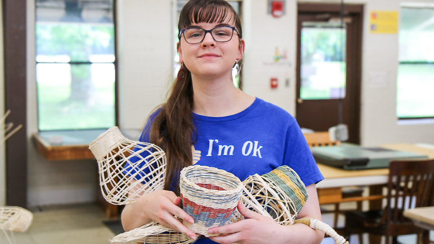 A student posing with three art pieces. 