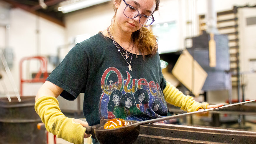 A student blowing glass in the glass studio.