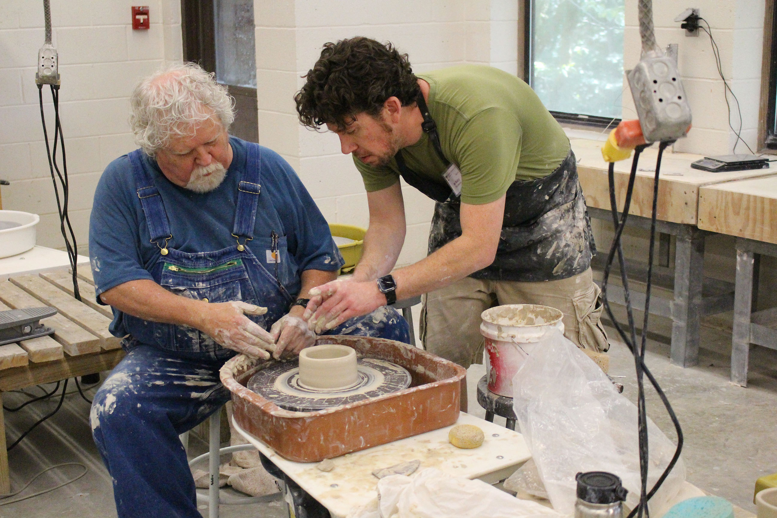 Instructor showing student how to work clay on a spinning table