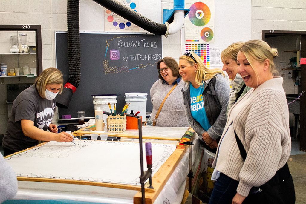 A group of women smiling and laughing as they learn a craft