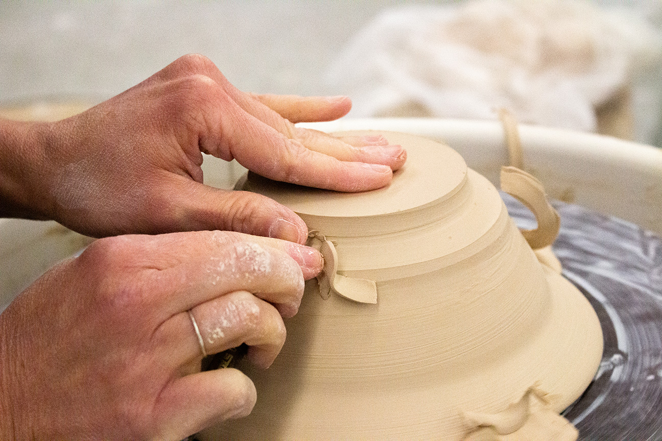 Hands carving a clay bowl on the wheel