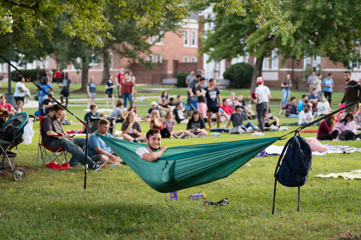 Student in hammock watch movie on quad.
