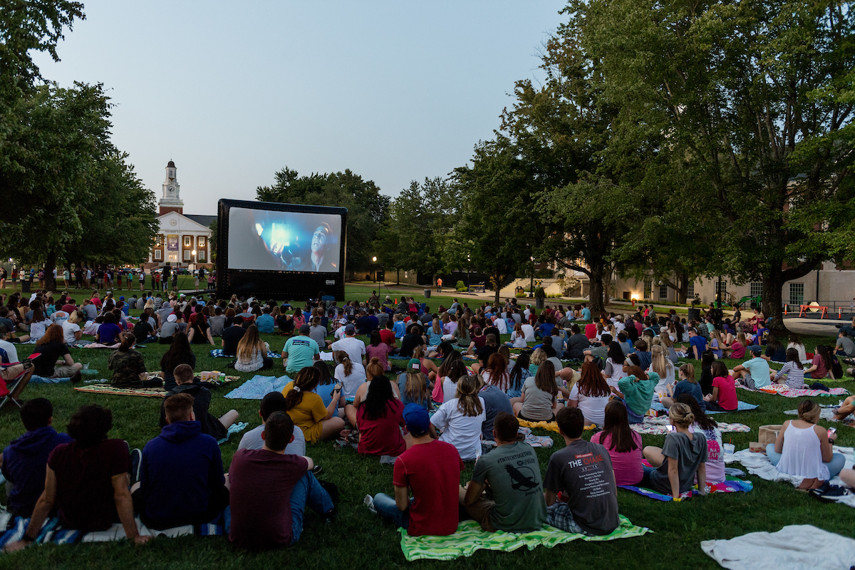 Students sitting on the quad watching a movie.