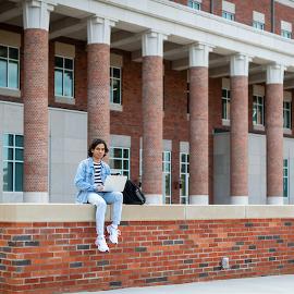 A student sitting on a ledge at LSC working on his computer.