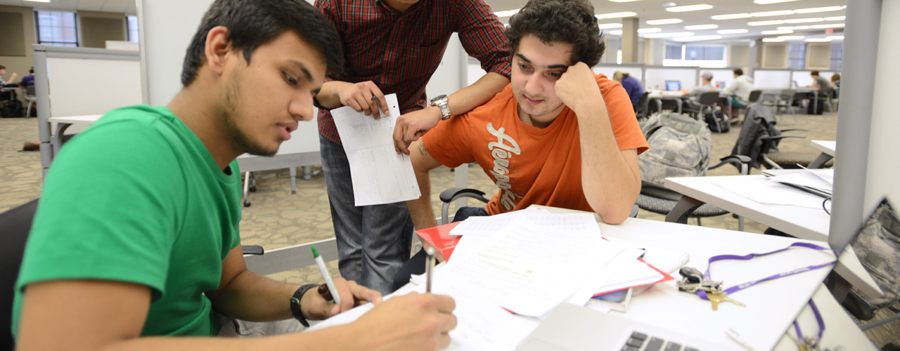 Three male students study notes at a desk in the library.