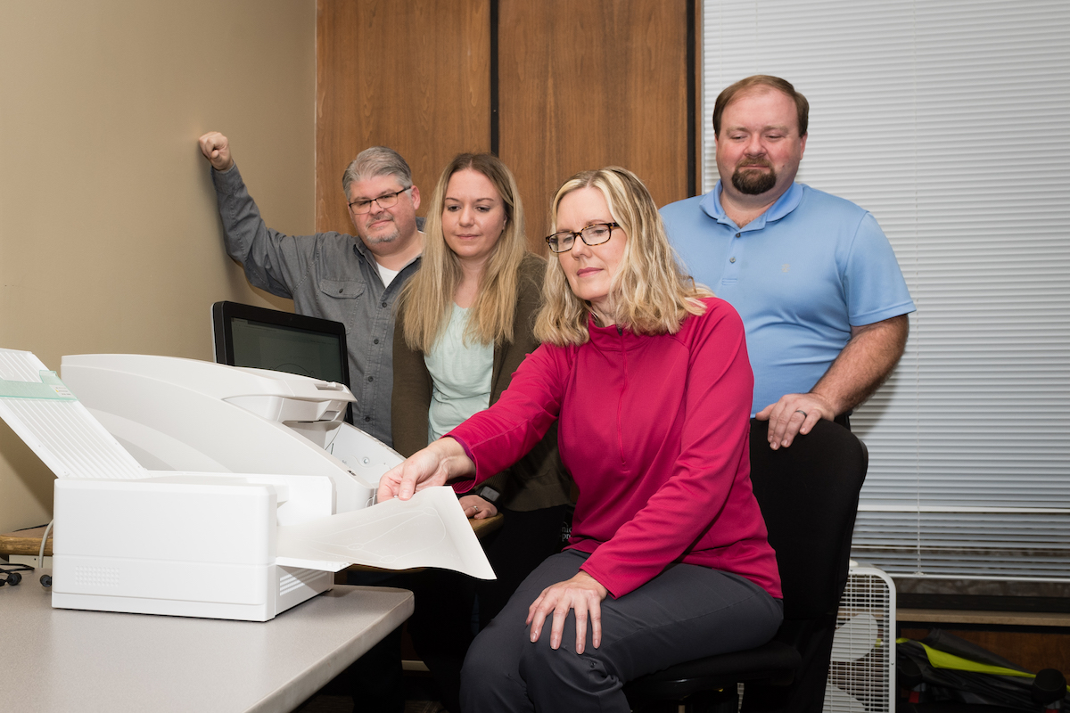 AEC Student Support associate Birgit Hoffman, seated, feeds some paper through a printer that creates tactile surfaces for visually impaired students to utilize while, from left, Chester Goad, AEC director; Tambra Sweet, coordinator; and Ed Beason, assistant director, look on.