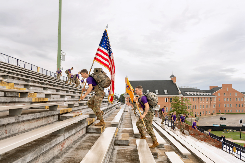 ROTC cadets climb stairs in Tucker Stadium while carrying an American flag.