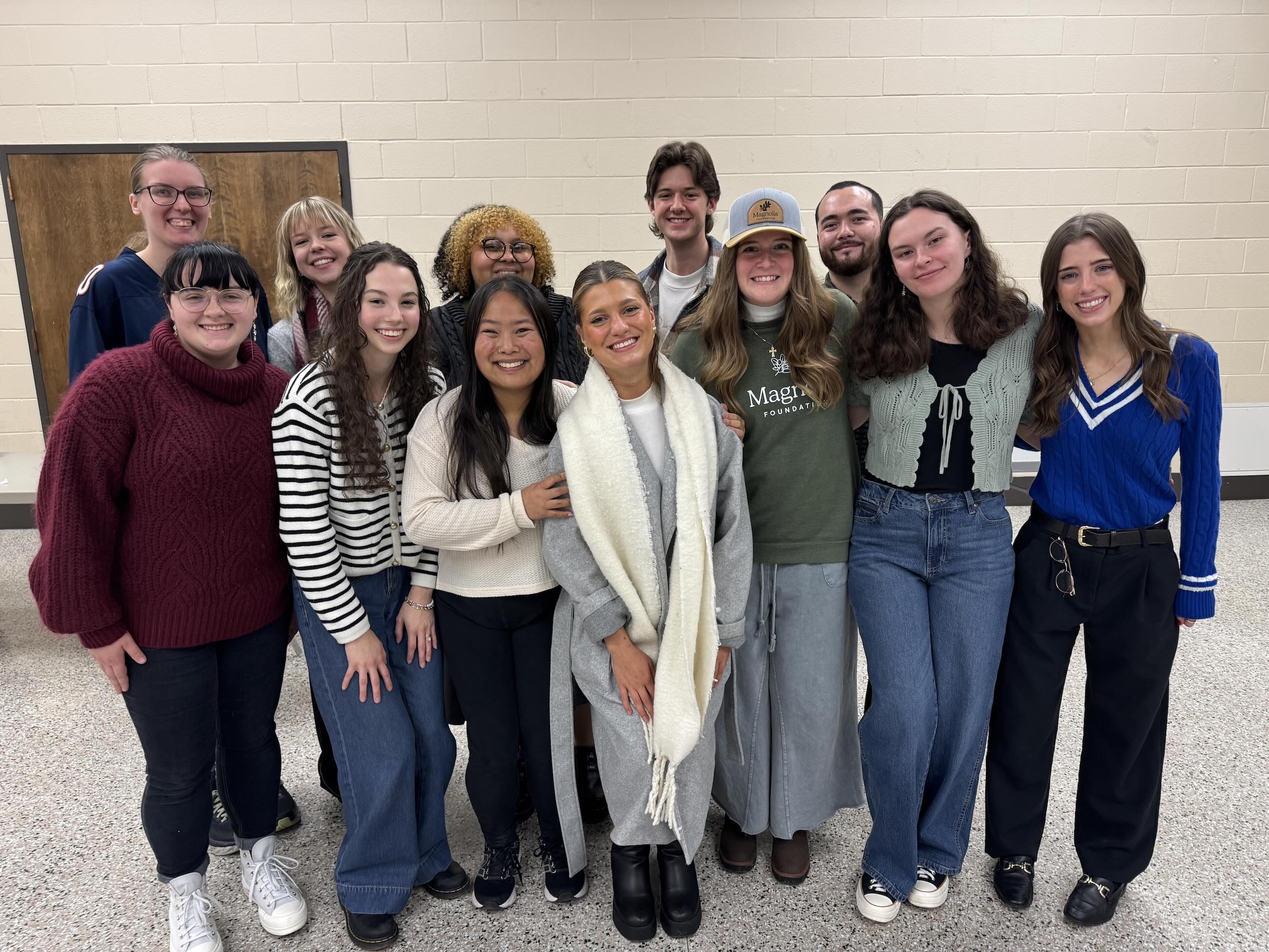 A group photo of students smiling in front of a white wall. 