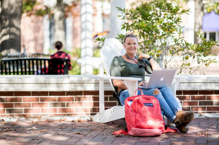 Phone of a student sitting in an adirondack chair in the shade on Tech's Centennial Plaza.