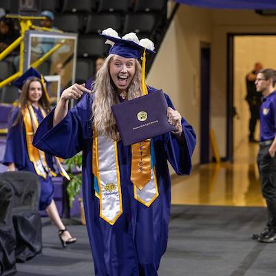 A student celebrating her graduation at commencement by pointing at her deploma cover.