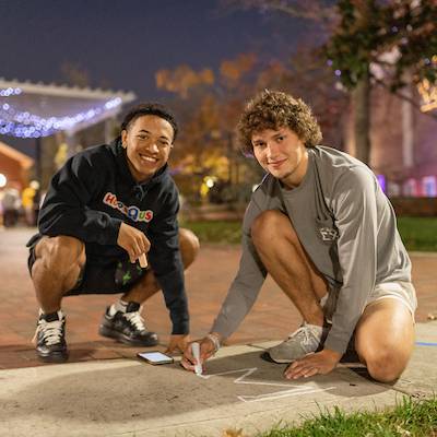 Two students chalking a sidewalk during a night event.