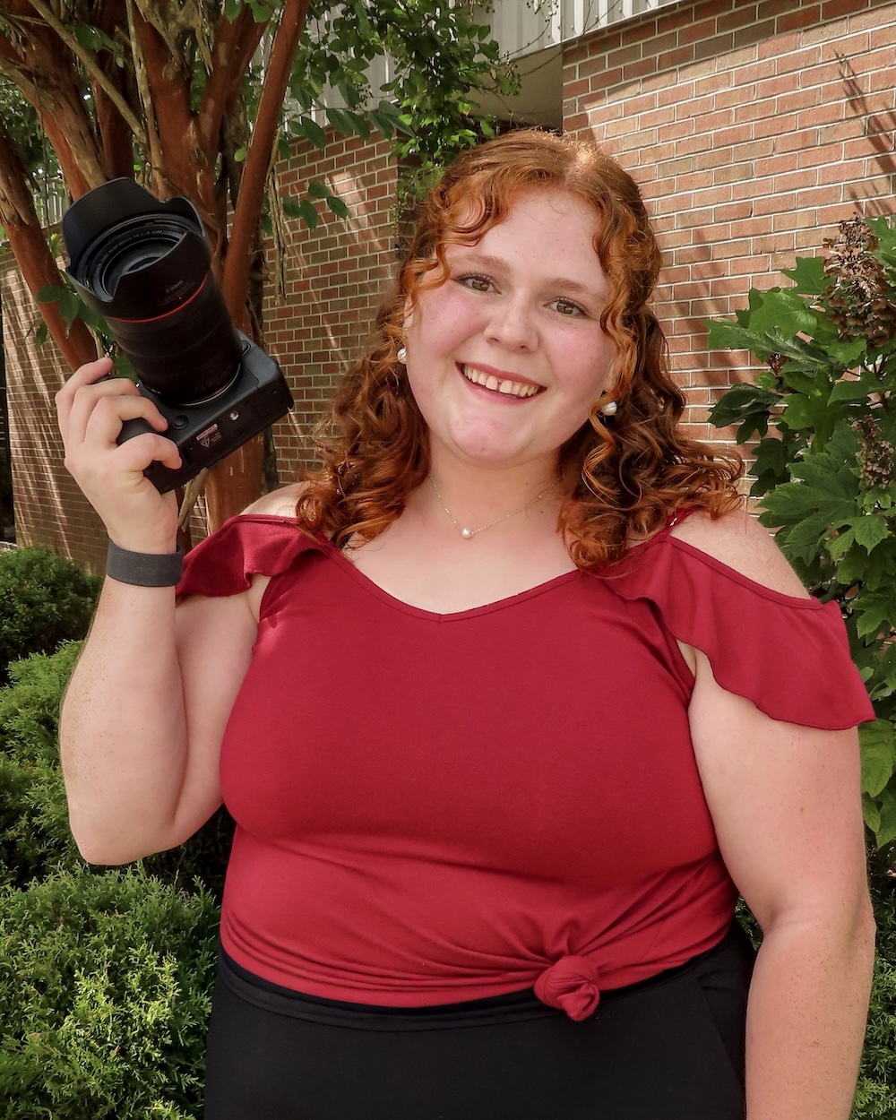 Student Lilly Davis stands holding a camera.
