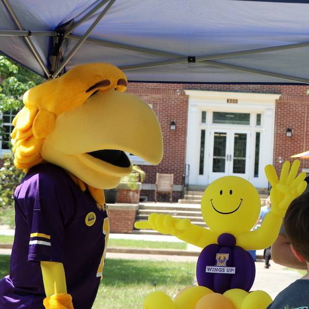 Awesome thinks Anthony makes some really amazing balloon art! He's looking at a figure of a little yellow balloon person riding a purple balloon tricycle.