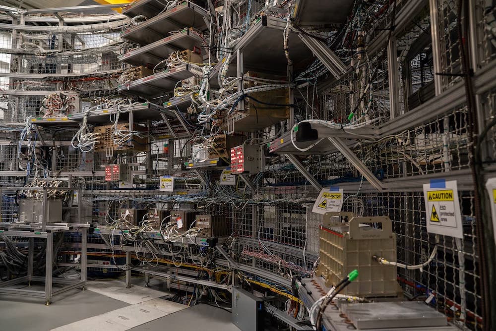 Marshall Space Flight Center Integration Lab - many wires and cables are running around the room, which is surrounded by a metal cage. 