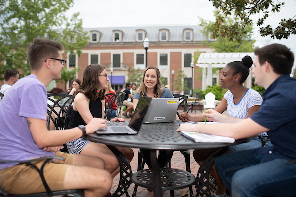 A group of students sitting outside on the plaza with a laptop.