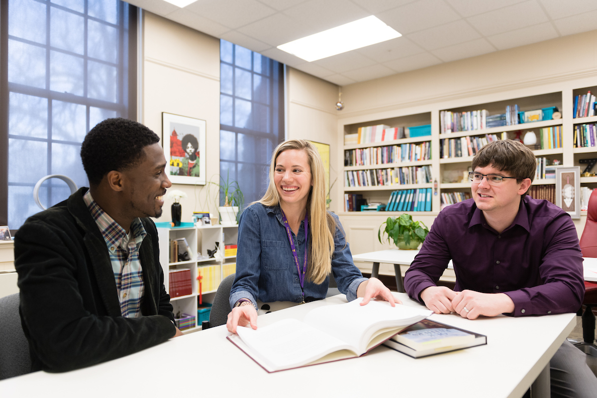 A group of students sit at a table smiling at each other