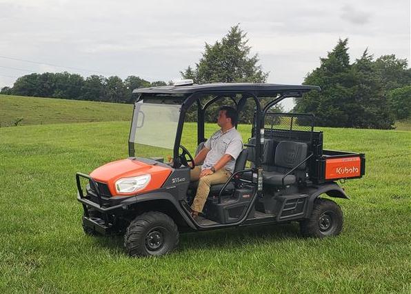 A man sits in a red and black side-by-side work vehicle. 