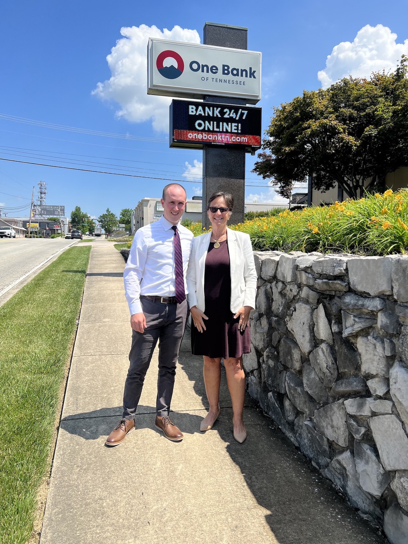 A man and woman stand on a sidewalk in front of the One Bank sign