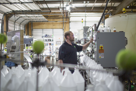 Photo of Adam Pogue checking equipment in his laboratory. Numerous plastic liquid fog bottles are in the foreground of the photo.