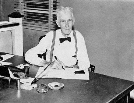 A black and white photo of Alvin G. Maxwell sitting at a desk holding the pen.