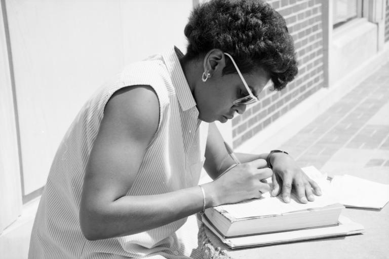 A snapshot of an african-american female student writing at an outdoor table.