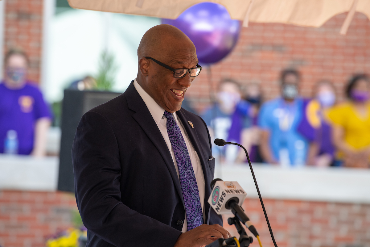 A photo of Marc Burnett at the grand opening of the new fitness center. He is smiling and standing at a lecturn.