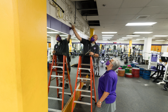 Photo of someone on a ladder unplugging a neon sign while another person looks on.