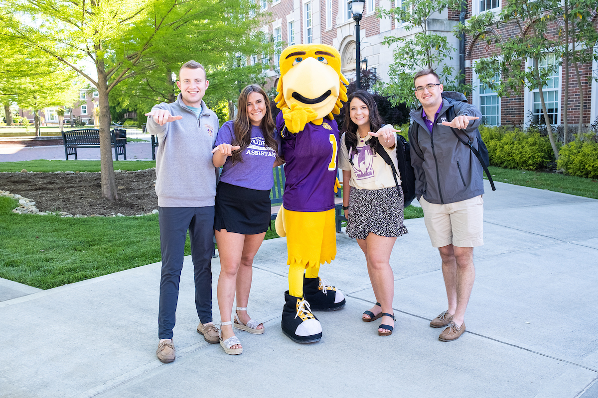 Several students stand around Awesome Eagle on Centennial Plaza. All are making the "wings up" sign at the camera.