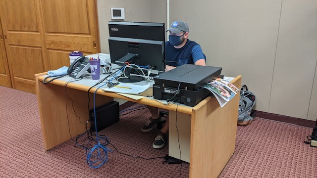 A masked student sits at a computer and scanner.