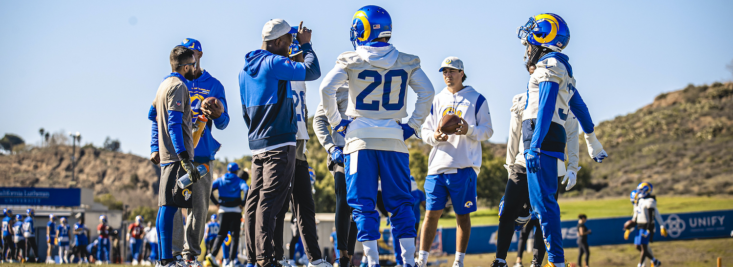 Football players and staff stand and talk on the field