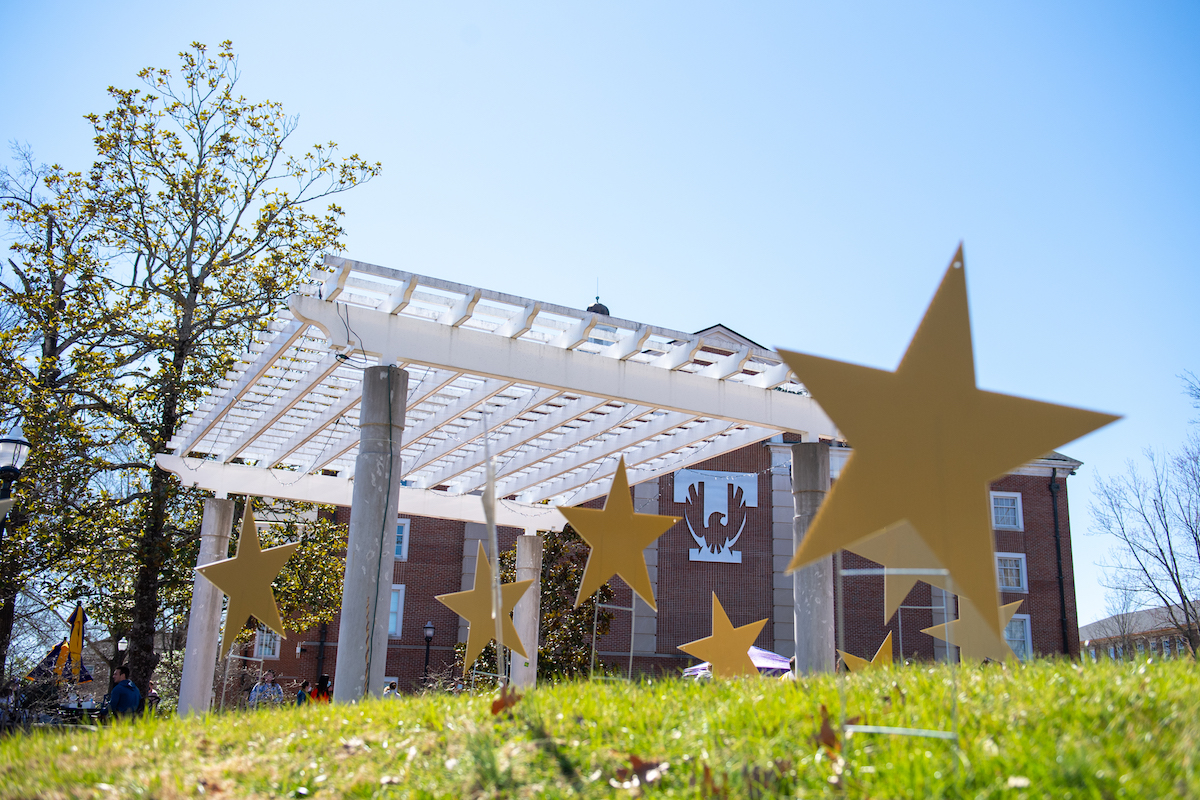 A low angle shot of the north side of Derryberry Hall. Mutliple stars are in the grass with a white pergola behind them.