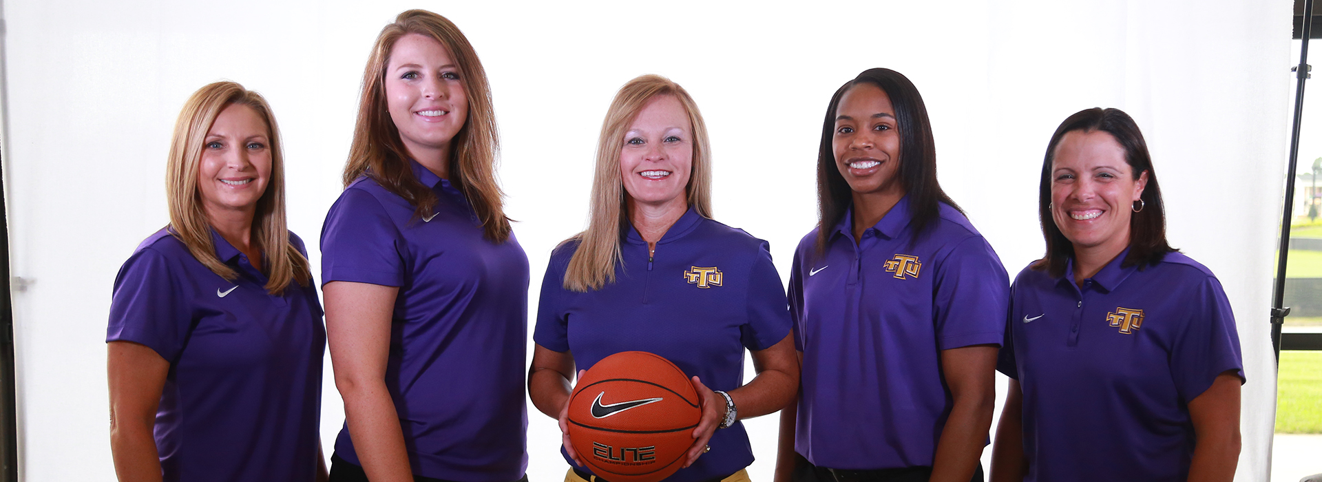 Women smiling at the camera in purple polo shirts.