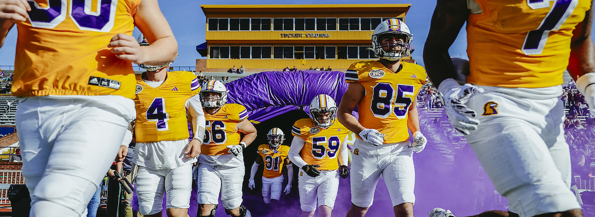 The football team running towards the viewer with the President's Box visible behind them.