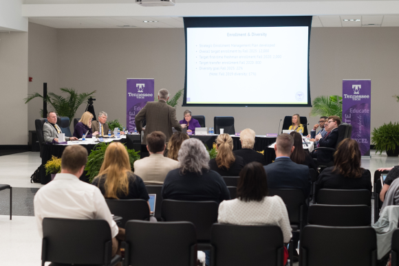 Photo President Phil Oldham standing at a podium and addressing the Board of Trustee in the multi-purpose room. 