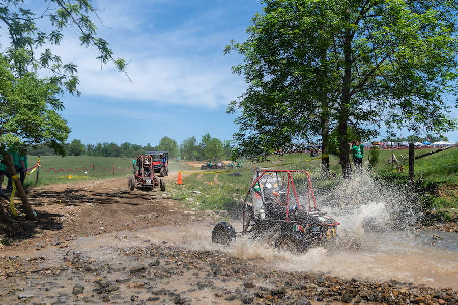 A baja vehicle splashes through mud on a track.