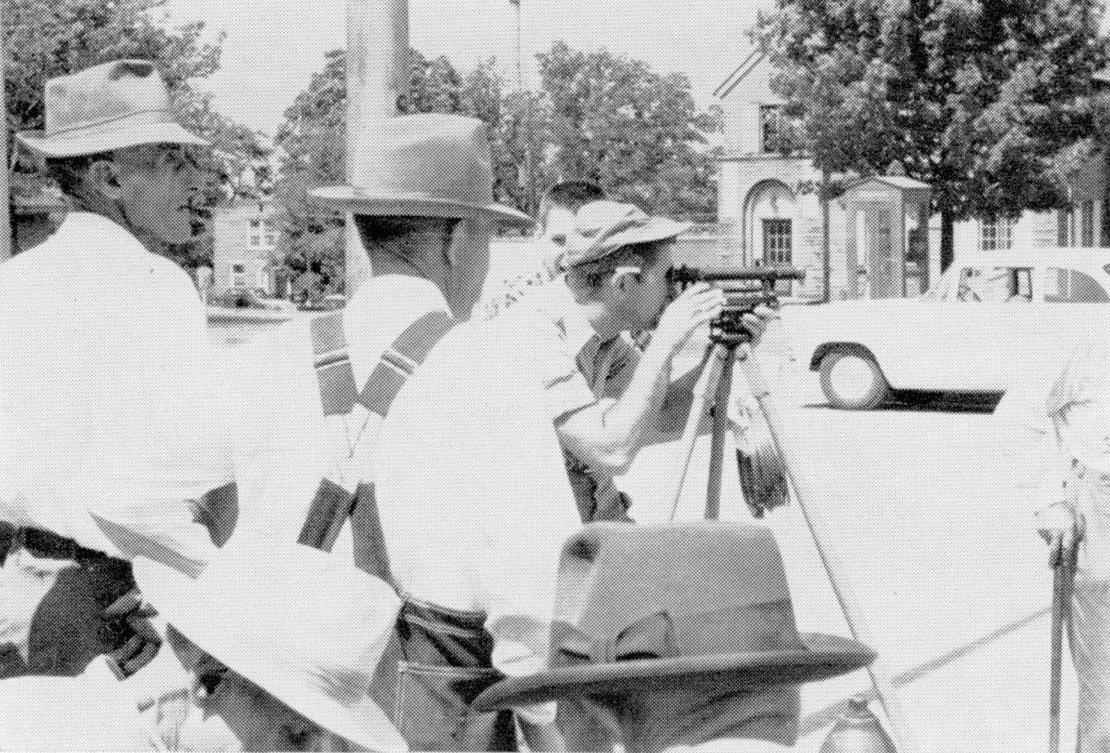 A black and white photo of a group of men seeming to be performing a survey