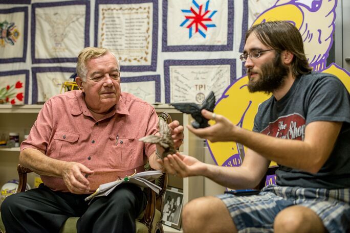 Tom Moran sits next to a student looking at small sculptures of the infamous eagle. 