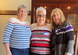 Nancy Holland, Lisa Bowen Field, and Donna Martin stand with their arms around each other while smiling at the camera